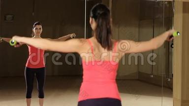 运动的女人用哑铃抬高肌肉。 健身模特照镜子。